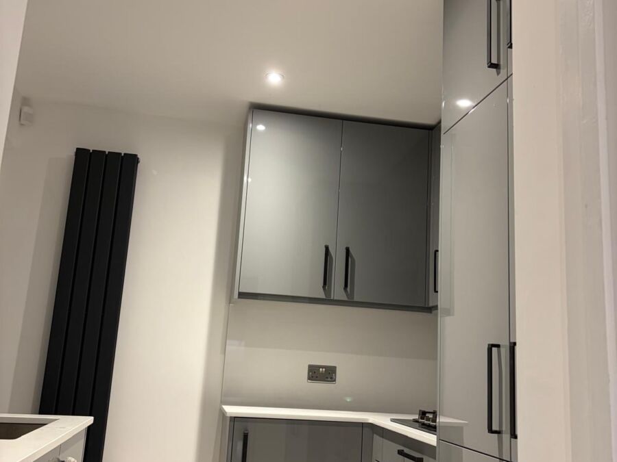 Modern fitted kitchen area with grey gloss wall and base units featuring black handles, white worktop, and integrated appliances