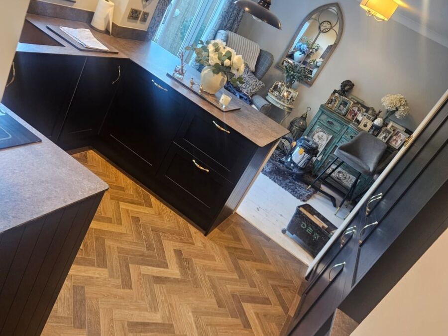 Open plan kitchen and dining area featuring herringbone parquet flooring in natural oak, black gloss handleless base units with dark worktops