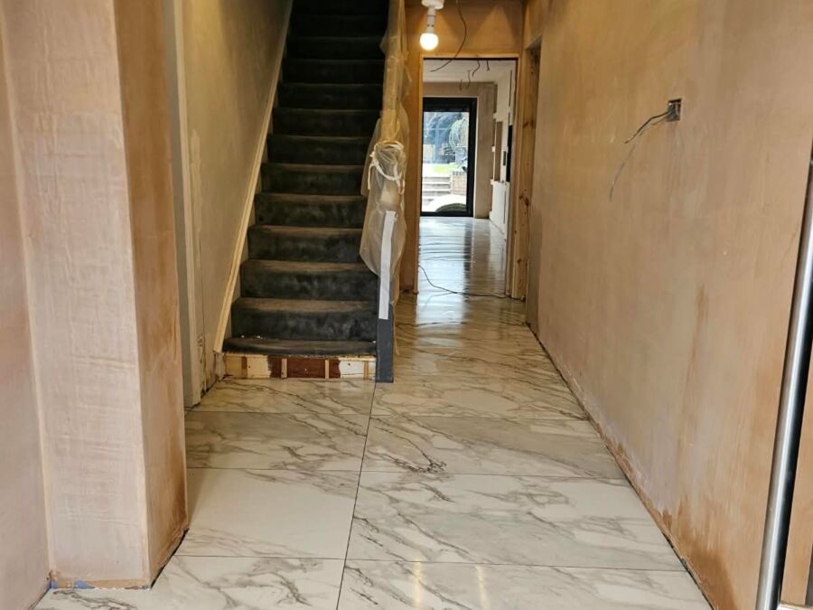 Residential hallway and staircase during renovation showing marble effect floor tiles, plastered walls awaiting decoration