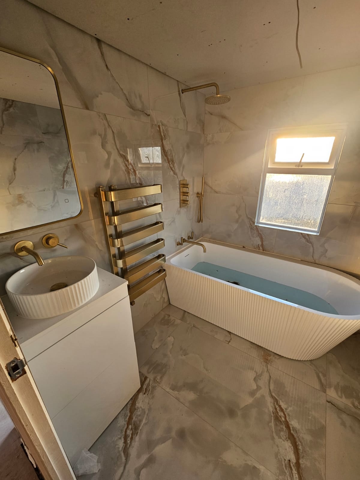 Luxury bathroom with black marble effect porcelain tiles and backlit mirror, finished by Brooks Construction
