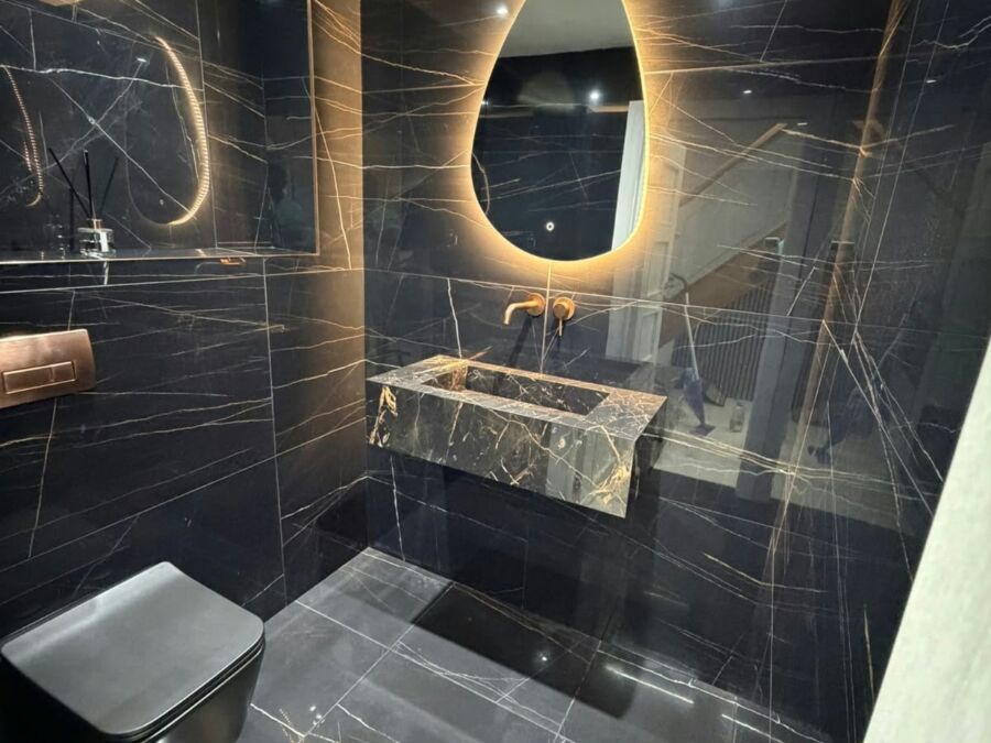Modern bathroom featuring large format black marble effect porcelain tiles on walls and floor, with a floating marble vanity basin